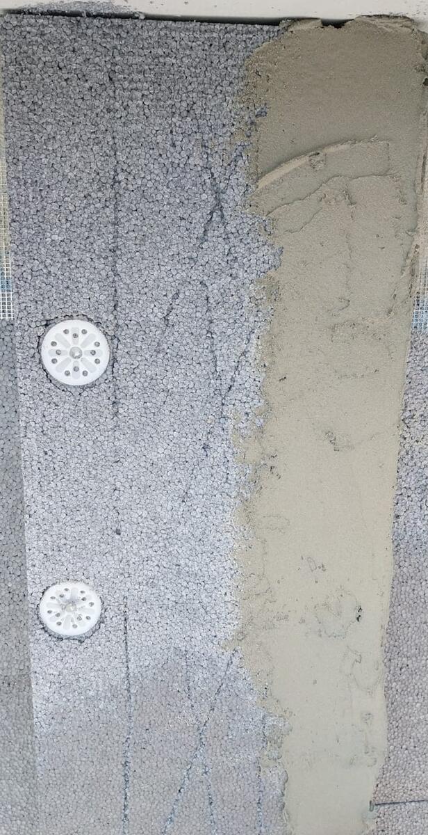 Dettaglio di tassellatura del pannello isolante in EPS con rasatura armata in corso su cappotto termico