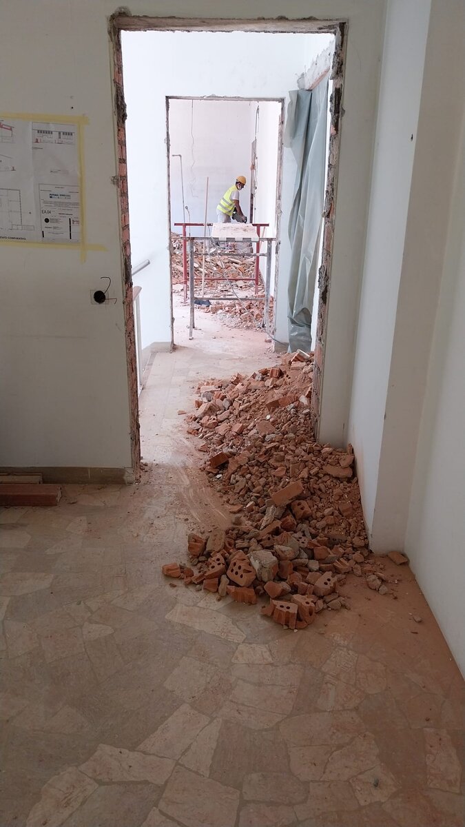 Demolizione di tramezzi in laterizio con macerie a terra e operaio al lavoro